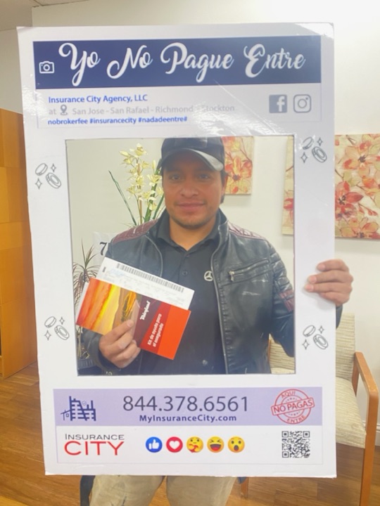 Stockton auto insurance customer Gustavo at Insurance City Stockton office holding Yo No Pague Entre testimony frame and new policy