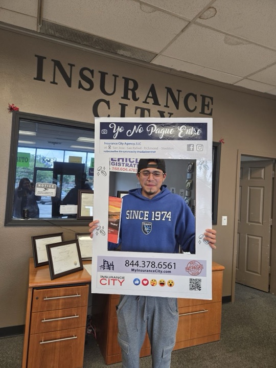 Stockton driver in Insurance City Stockton lobby holding Yo No Pague Entre frame — proof of no broker fee policy